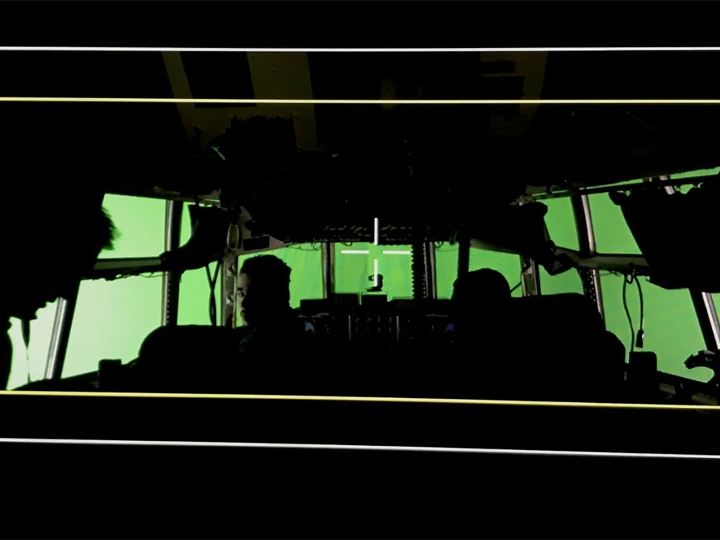 Film set featuring a green screen backdrop with crew members in silhouette.