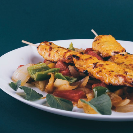 Delicious grilled chicken skewers served on a plate with sautéed vegetables and fresh herbs, against a green background.