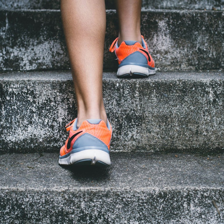 Close-up of a person wearing vibrant orange and gray sneakers walking up concrete stairs.