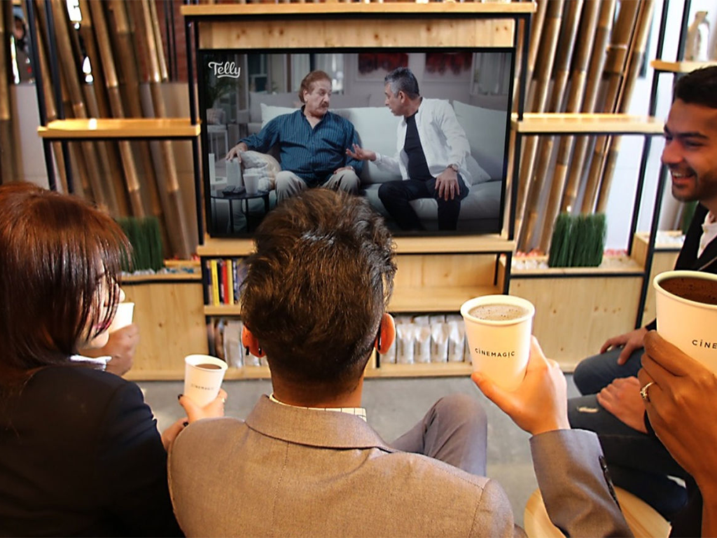 Group of people enjoying a show on a screen in a cozy setting with cups in hand, showcasing the Cinemagic experience.